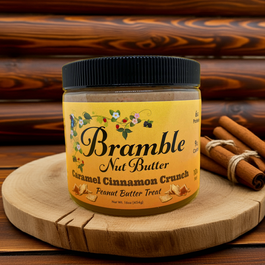 Jar of Bramble Nut Butter Caramel Cinnamon Crunch on a wooden surface with cinnamon sticks.